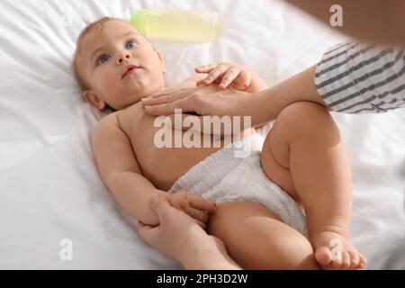 Mutter massiert ihr süßes Baby mit Öl auf dem Bett Stockfoto
