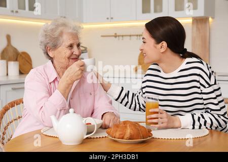 Junge Pflegekraft und Seniorin frühstücken am Tisch in der Küche. Häusliche Pflege Stockfoto