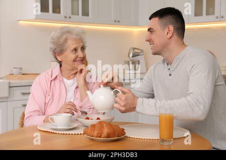 Junge Pflegekraft, die das Frühstück für Seniorin am Tisch in der Küche serviert. Häusliche Pflege Stockfoto