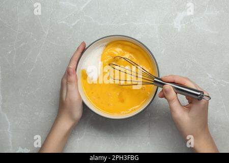 Eine Frau, die Eier am hellgrauen Tisch windet, Draufsicht Stockfoto