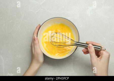 Eine Frau, die Eier in einer Schüssel am hellgrauen Tisch rührt, Draufsicht Stockfoto