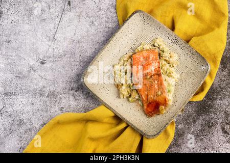 In Sahne gebackener Lachs mit Lauch auf einem quadratischen Teller auf dunkelgrauem Hintergrund. Draufsicht, flach liegend Stockfoto