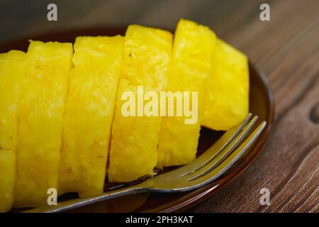 Nahaufnahme von geschnittenen frischen Sarawak-Ananas (Smooth Cayenne) auf einer dunkelbraunen Untertasse auf einem Holztisch Stockfoto