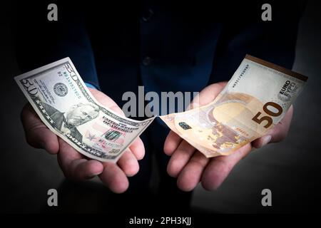 Das Konzept der Wahl zwischen Dollar und Euro. Banknoten von 50 Euro und 50 Dollar in den Händen eines Geschäftsmannes auf dunklem Hintergrund. E Stockfoto