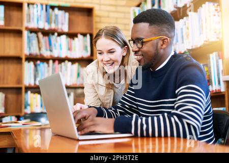 Sie sind wirklich gute Lernfreunde. Ein junger Mann schaut zu, während eine Studentin an einem Laptop arbeitet. Stockfoto