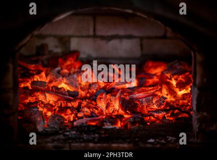 Flamme des Feuers von heißen brennenden Kohlen im Kamin. Wärme aus dem Ofen. Stockfoto