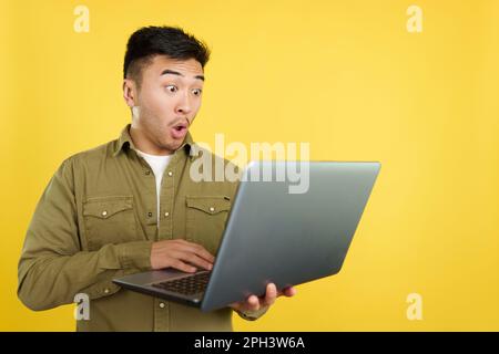 Ein Chinese mit einem überraschten Aussehen, der einen Laptop benutzt Stockfoto