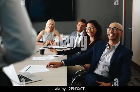 Glückliche Geschäftsleute lächeln, während sie in einem Sitzungssaal sitzen und einer Rede zuhören. Erfolgreiche Unternehmensprofis mit einem Stockfoto