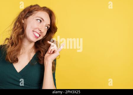 Glückliche rothaarige Frau, die einen leeren Platz zur Seite zeigt Stockfoto