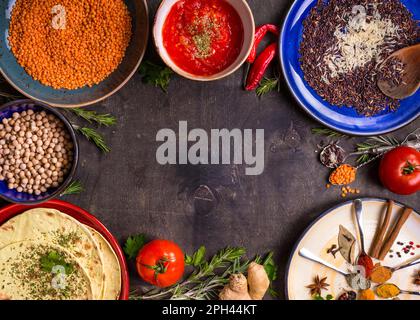 Traditionell für asiatische oder östliche Küche Getreidekörner, Bohnen, Gewürze auf bunten Tellern/Linsen, Reis, Kichererbse, Tomaten-Chutney, Pita. Zutaten Stockfoto