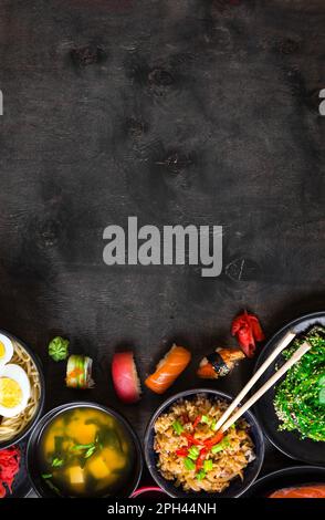 Sushi und japanische Speisen auf dunklem Hintergrund. Sushi-Brötchen, Hiyashi Wakame, Miso-Suppe, Ramen, gebratener Reis mit Gemüse, Nigiri, Lachs-Steak, Soja Stockfoto