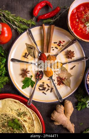 Verschiedene Gewürze, Kräuter, Kichererbse, Linsen, Basmati und wilder Reis, Tomaten-Chutney und Pita auf bunten Tellern. Draufsicht. Gewürze und anders Stockfoto