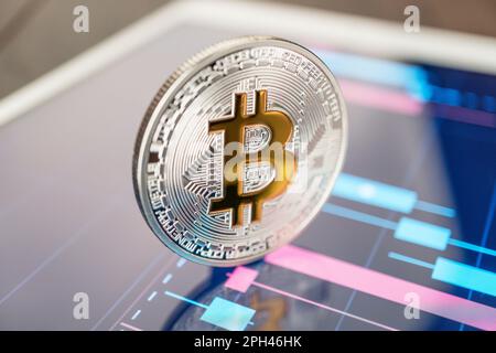 Nahaufnahme einer Bitcoin-Kryptowährung-physischen Münze auf dem Tablet-Computer mit Aktienkarten. Der Handel mit Bitcoin Cryptocoin-Konzept auf der W. Stockfoto