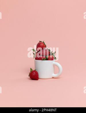 Frisch gepflückte, saftige Erdbeeren der Saison im Becher auf pinkfarbenem Hintergrund Stockfoto