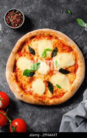 Italienische Pizza Margherita mit Mozzarella und Basilikumblättern im dunklen Hintergrund, frisch gebackene Pizza Stockfoto