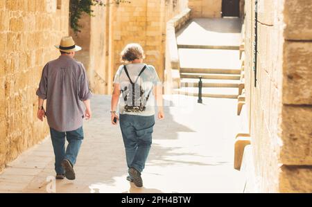 Ein nicht wiedererkennbares, reifes, weißes Paar von Touristen, die durch ein typisches mediterranes Dorf laufen - mit Rucksack und strohhaltigem panamahut Stockfoto