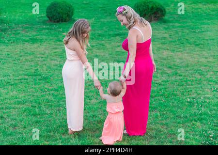 mom mit zwei Töchtern in ähnlichen Kleidern geht im Park spazieren Stockfoto