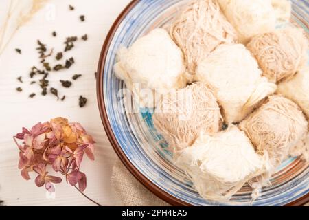 Traditionelle arabische Süßigkeiten Pishmanie und eine Tasse grüner Tee auf weißem Holzhintergrund und Leinentextilien. Draufsicht, flach liegend, Nahaufnahme. Stockfoto