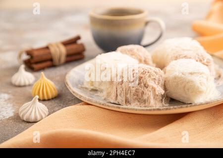 Traditionelle arabische Süßigkeiten pishmanie und eine Tasse Kaffee auf braunem Betonhintergrund und orangefarbenem Leinentuch. Seitenansicht, Nahaufnahme, selektiver Fokus. Stockfoto
