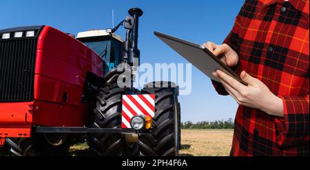 Ein Landwirt mit einem digitalen Tablet steuert einen autonomen Traktor auf einem intelligenten Betrieb. Hochwertiges Foto Stockfoto