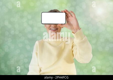 Eine Frau hält ein Telefon mit einem leeren Display in der Hand. Abstrakter Hintergrund. Hochwertiges Foto Stockfoto
