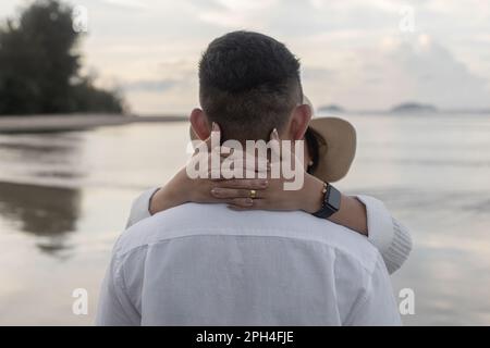 Die Hände der Frau mit einem überkreuzten goldenen Ring um den Hals ihres Partners. Stockfoto
