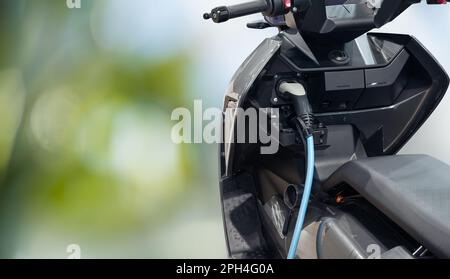 Elektrischer Roller mit angeschlossenem Ladekabel auf grünem Hintergrund. Hochwertiges Foto Stockfoto