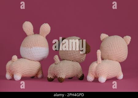 Süßes kleines Kätzchen, Hündchen und Kaninchen gestrickt, handgemachte Kunst. Rückansicht. Amigurumi drei Tierpuppen auf pinkfarbenem Hintergrund. Heimwerker-Spielzeug aus natürlichem Material Stockfoto