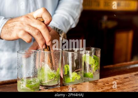 Ein erfahrener Barkeeper bereitet fachkundig einen traditionellen kubanischen Mojito-Cocktail mit Minzblättern und Limettenspalten zu. Stockfoto