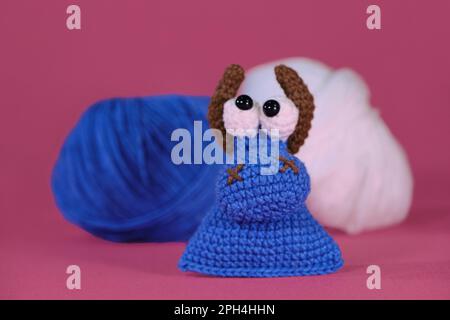 Amigurumi ein kleiner blauer Stier mit braunen Hörnern auf rosa Hintergrund mit blau-weißen Fadenbällen. Weiches Spielzeug aus natürlicher Baumwolle und Wolle. C Stockfoto