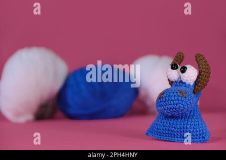 Weiches Spielzeug aus natürlicher Baumwolle und Wolle. Kuhkopf gestrickt, handgemachte Kunst. Amigurumi, ein kleiner blauer Stier mit braunen Hörnern auf rosa Hintergrund Stockfoto