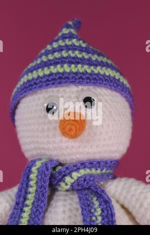 Weiches Spielzeug aus natürlicher Baumwolle und Wolle. Gestrickt, handgefertigt. Amigurumi, ein kleiner weißer Schneemann mit orangefarbener Nase und gestreiftem Hut und Schal Stockfoto