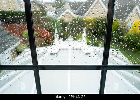 Flacher Fokus von Regentropfen, wenn man aus einem Schlafzimmer-Fenster im oberen Stockwerk schaut. Ein großes Wintergarten ist unten zu sehen, eingerahmt von der Führung. Stockfoto