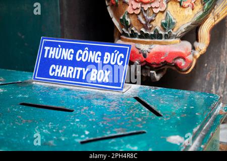 Grüne Spendenbox mit einem Schild auf Vietnamesisch und Englisch in einem Tempel. Eine Wohltätigkeitsbox mit mehreren Schlitzen, um Geld für eine Sache anzubieten Stockfoto