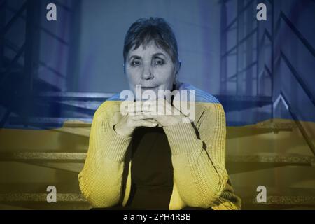 Doppelte Exposition der Nationalflagge und der Seniorin, die auf der Treppe sitzt. Beenden Sie den Krieg in der Ukraine Stockfoto