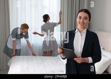 Housekeeping Manager mit Tablet, um die Arbeit der Zimmermädchen im Hotelschlafzimmer zu überprüfen Stockfoto