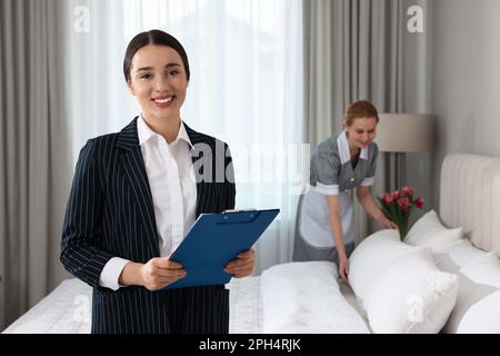 Housekeeping Manager mit Klemmbrett überprüft die Arbeit der Zimmermädchen im Hotelzimmer Stockfoto