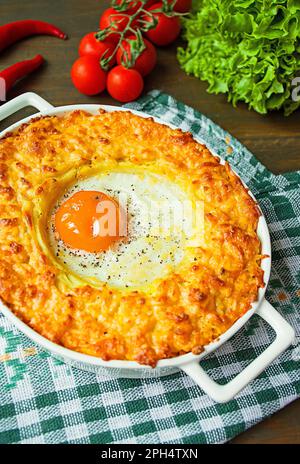 Kartoffelauflauf mit Bolognese. Auflauf für gebackene Kartoffeln mit Ei und geriebenem Käse in einem keramischen, ovalen Backblech. Dunkler Holzhintergrund. Ansicht von einem Stockfoto