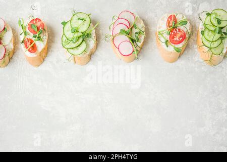 Verschiedene vegetarische Sandwiches mit Gemüse und Kräutern auf hellem Hintergrund. Richtige Ernährung. Diät-Nahrung. Lebensmittelhintergrund. Draufsicht. Speicherplatz kopieren. Stockfoto