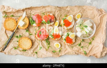 Canapés mit rotem Kaviar und Canapés mit rotem Fisch sind mit Mikro-Grüns dekoriert, Wachteleier sind auf Papier. Stockfoto