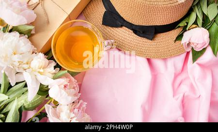 Ein Rahmen aus weißen und pinkfarbenen Pfingstrosen, ein Frauenhut, eine Tasse Tee auf pinkfarbenem Stoffhintergrund. Frühlings- oder Sommerkonzept mit Blumendesign. Flach liegend. Blick von oben. Stockfoto