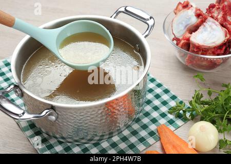 Köstliche hausgemachte Knochenbrühe und Zutaten auf einem Holztisch Stockfoto