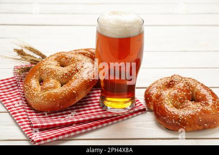 Ein Glas Bier und leckere frisch gebackene Brezeln auf einem weißen Holztisch Stockfoto