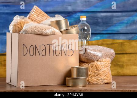 Spendenbox, verschiedene Produkte und ukrainische Flagge im Hintergrund. Hilfe während des Krieges Stockfoto