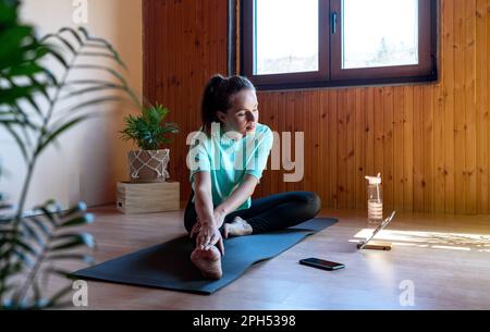 Junge Erwachsene Frau sitzt auf Yogamatte und dehnt ihren Körper. Stockfoto