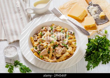 Thunfisch-Pilz grüne Erbsen-Fusilli-Auflauf mit cremiger Käsesauce in weißer Schüssel, mit Zutaten auf dem Tisch Stockfoto