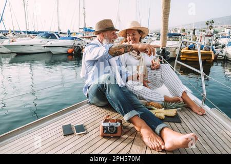 Seniorenpaar, das während der Sommerferien Champagner auf dem Segelboot trinkt - Fokus auf Männerhand Stockfoto