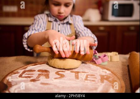 Details an den Händen des Kindes mithilfe einer Walznadel Rollen Sie den Teig aus, während Sie Osterkuchen in der Küche zubereiten Stockfoto