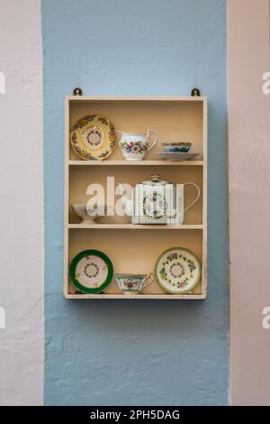 Ein Regal mit einer porzellan-Teekanne mit Blumenmuster, einem Milchkännchen und Untertassen. Teehaus oder Teestube. Stockfoto