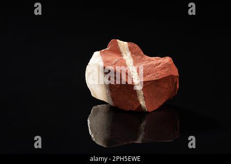 Roter, ungeschnittener, verformter Jasper mit transparentem Quarzmineralstein auf reflektierender schwarzer Oberfläche Stockfoto